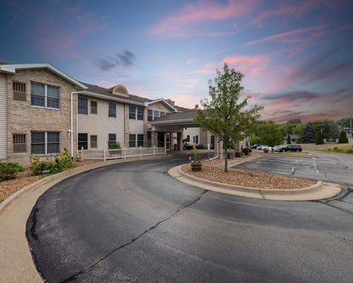 Entrance driveway of Sunset Park Place with trees and flowers.