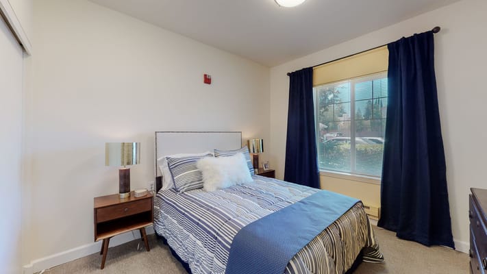 A well-decorated bedroom featuring a bed, nightstand, and curtains.