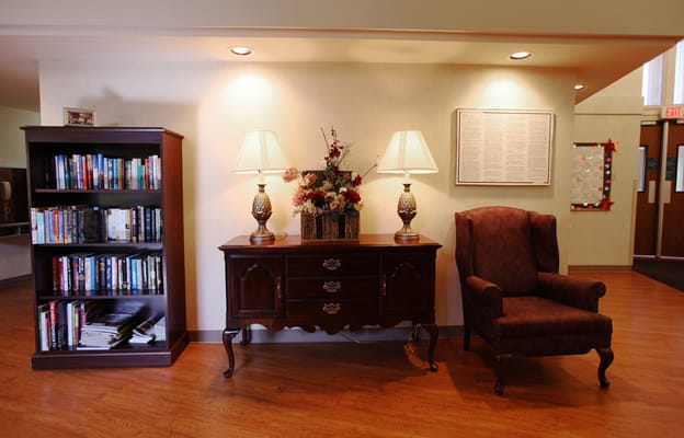 A lobby with a bookshelf, decorative lamp, and a comfortable armchair.