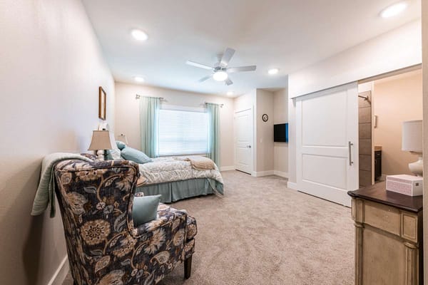 Spacious bedroom with bed, chair, and natural light.