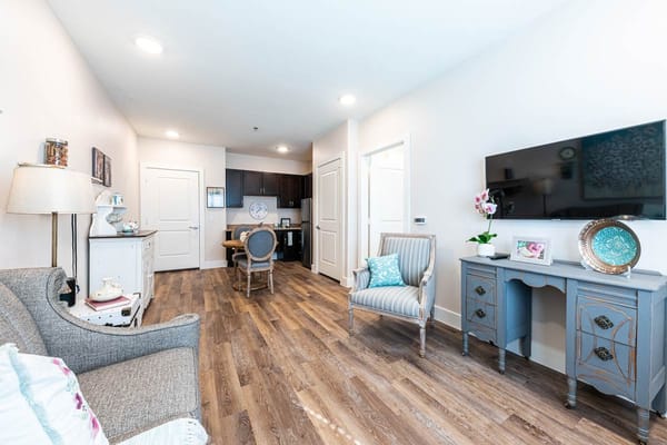 A comfortable living room with a couch, dining area, and TV in The Philomena facility.