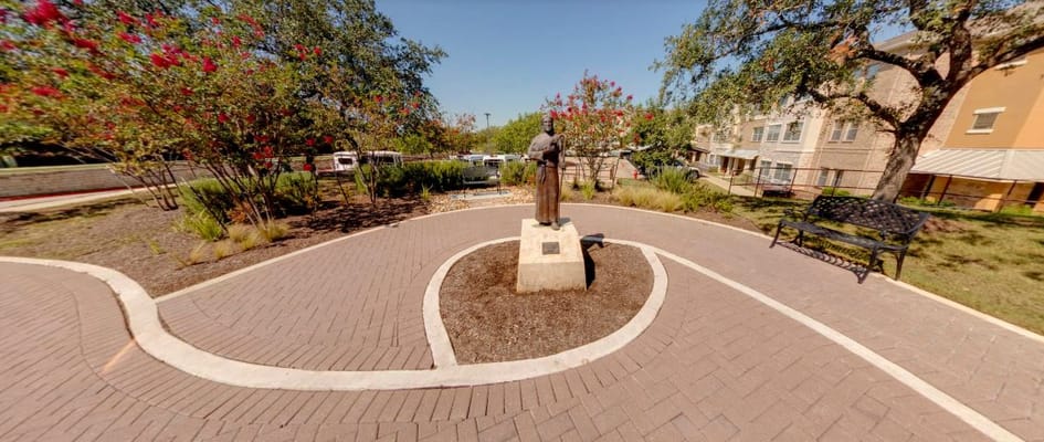 A bronze statue surrounded by flowering plants in a garden path.