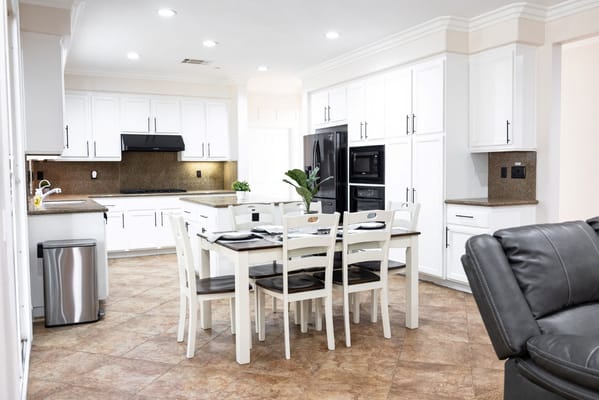 Brightly lit kitchen with white cabinetry and a dining table.