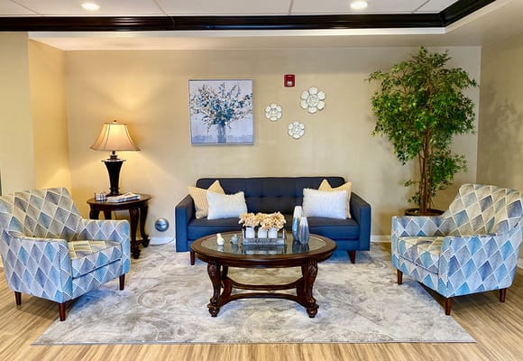 A welcoming living room with a blue couch, patterned chairs, and decorative plants.
