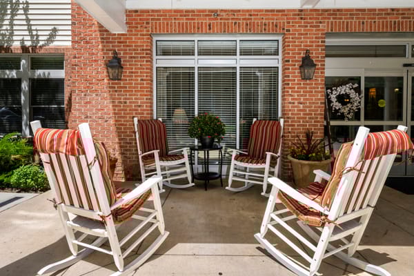 Four white rocking chairs with red striped cushions arranged around a small table.
