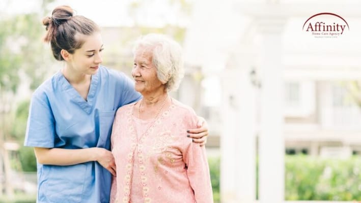 A caregiver assisting an elderly woman outdoors