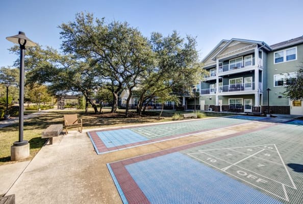 Outdoor courtyard with blue shuffleboard court and shaded seating