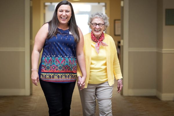 Staff and resident walking together, smiling in the hallway