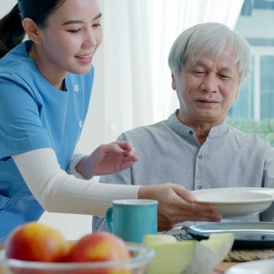 Staff serving food to a senior resident in a dining room