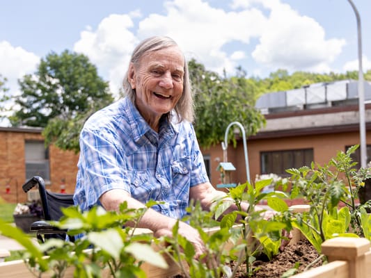 Elderly resident gardening outdoors, smiling.