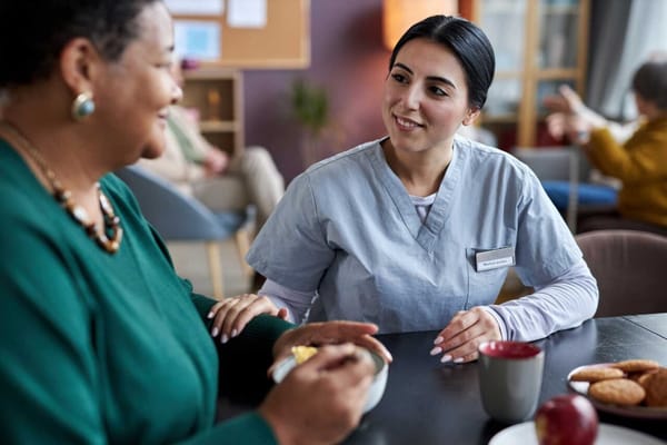 A caregiver and resident engaged in conversation indoors.