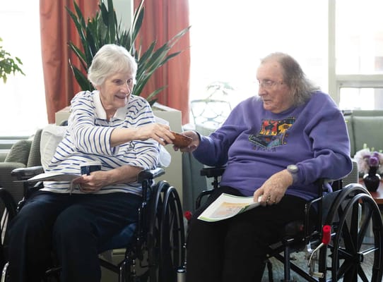 Two women in wheelchairs interacting in a common area