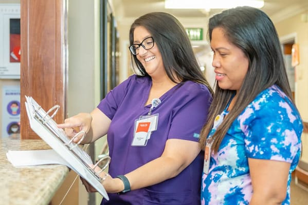 Two staff members reviewing a binder in a hallway