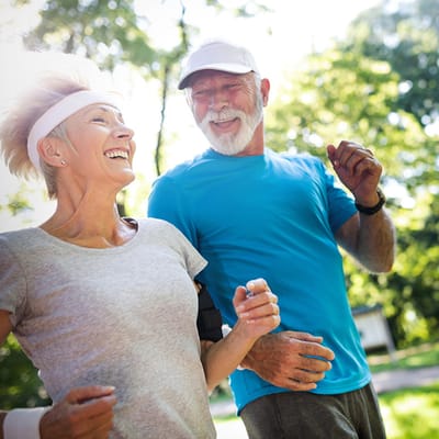 Two seniors jogging together outdoors, smiling and enjoying