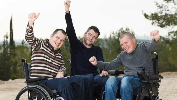 Three smiling men in wheelchairs celebrating outdoors