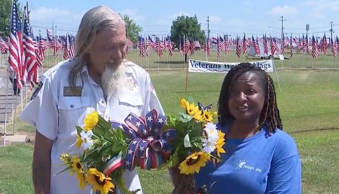 Two individuals presenting a flower arrangement in a field of flags