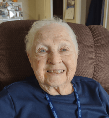 An elderly resident smiling warmly in a cozy chair