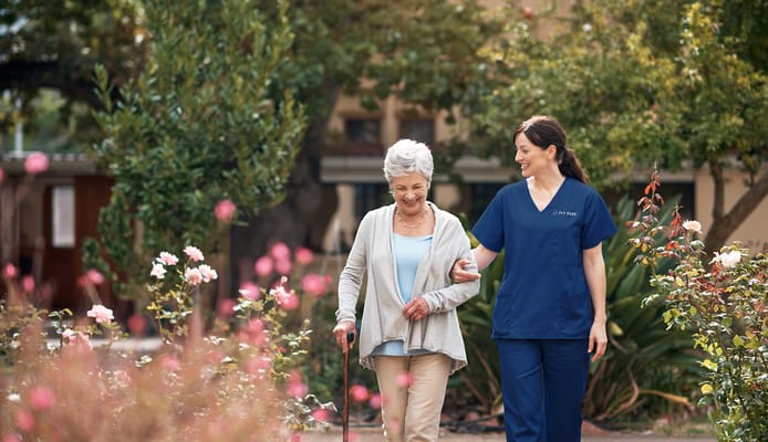 A caregiver walking with a resident in a garden