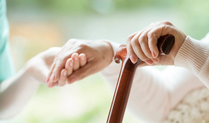 Hands of a caregiver and a senior holding a cane