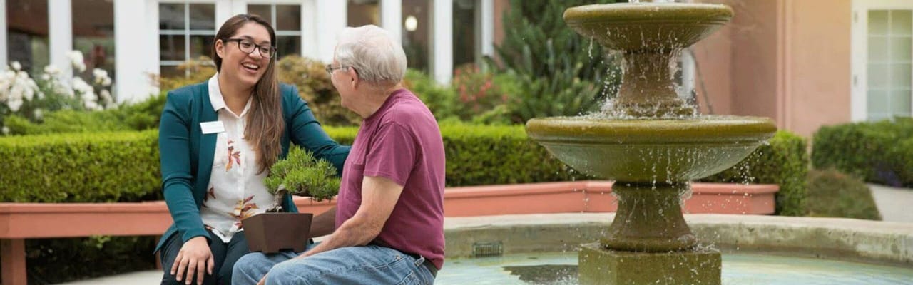 A resident and staff member chatting by a fountain in a garden