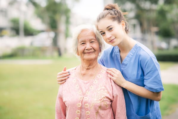 A caregiver and an elderly woman smiling outdoors