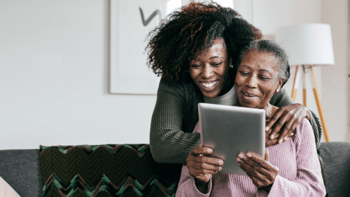 Two women happily using a tablet together in a cozy living space