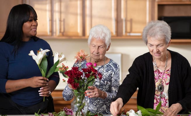 Residents and staff arranging flowers in a kitchen