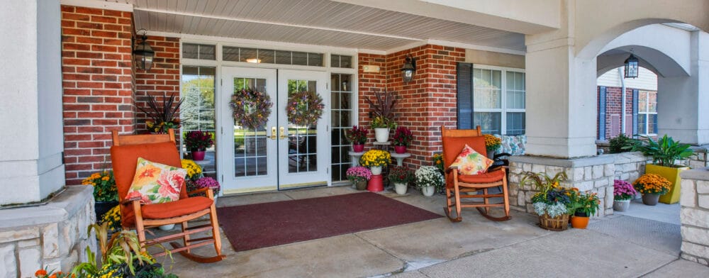 Entrance of a senior living facility with rocking chairs and flowers