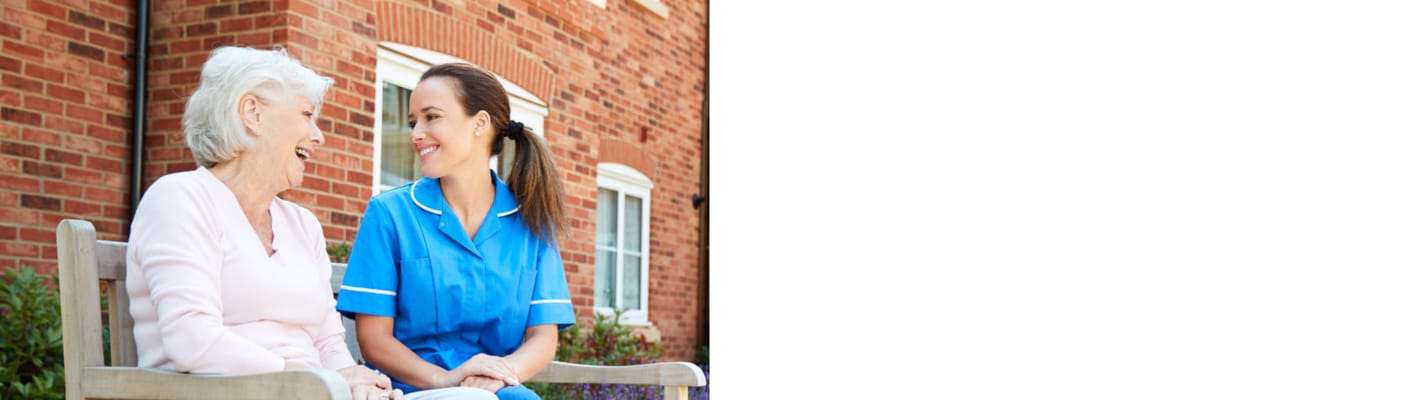A resident and staff member smiling together on a bench