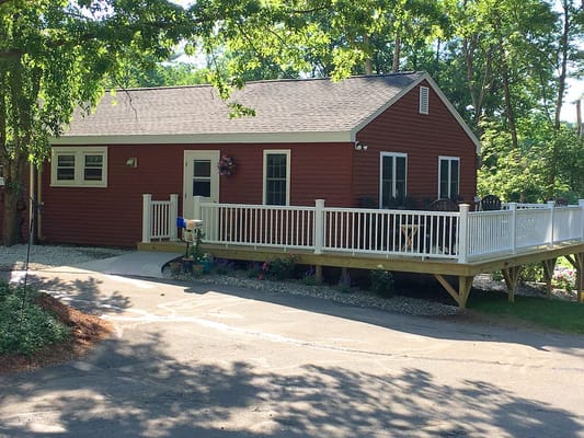 A red house with a white railing and outdoor seating area surrounded by trees