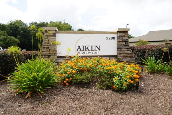 Entrance sign to Aiken Memory Care with landscaped flowers