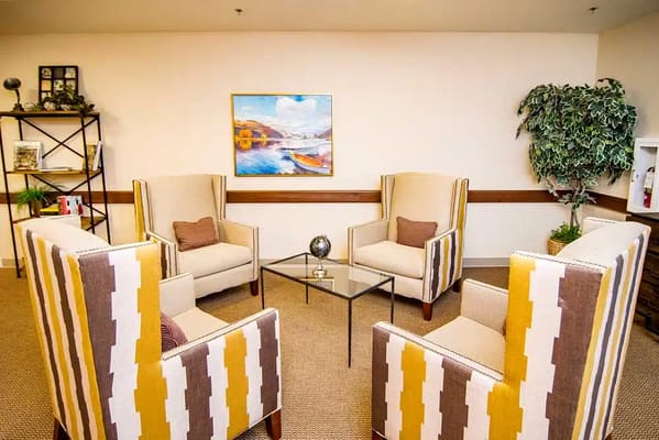 Four chairs and a coffee table in a cozy lounge area with a painting on the wall.