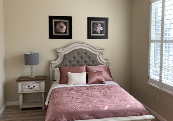 A cozy bedroom featuring a large bed, decorative pillows, nightstand, and lamps.