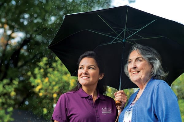 Caregiver and resident sharing an umbrella outdoors