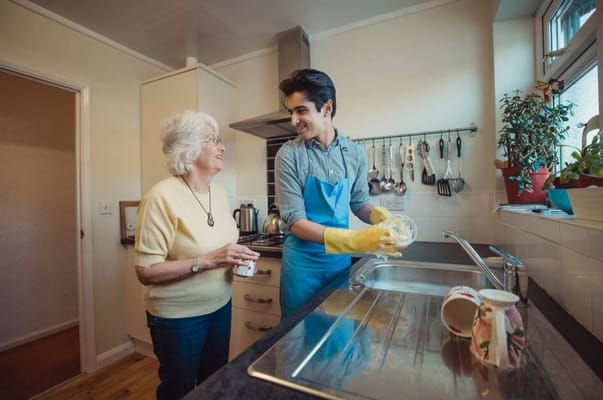 A caregiver smiling while helping a senior in a kitchen