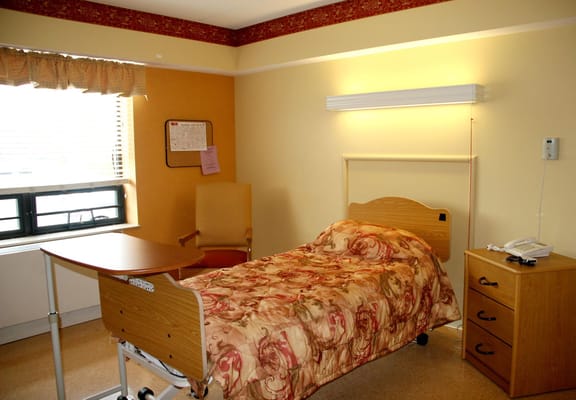 A well-furnished bedroom in a senior living facility with a bed, chair, and bedside table.