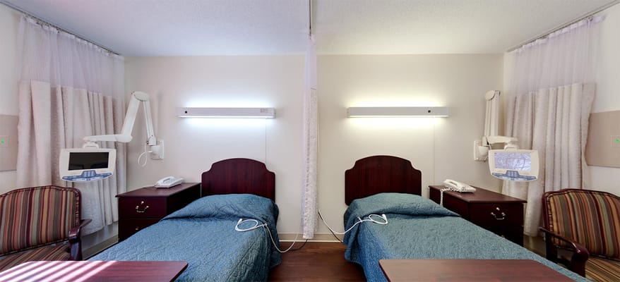 A shared bedroom with two beds, each equipped with phone and light fixtures.
