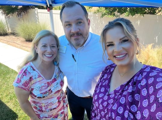Three staff members posing together outside in a garden setting