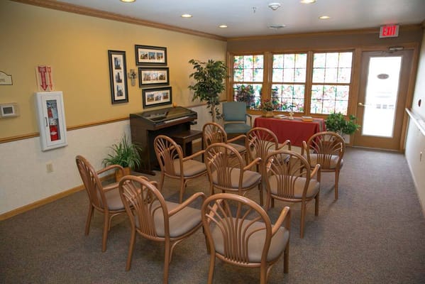 Empty seating arranged in a common area with a piano and stained glass windows.