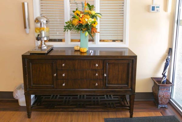 A wooden sideboard with a decorative flower arrangement and a beverage dispenser.