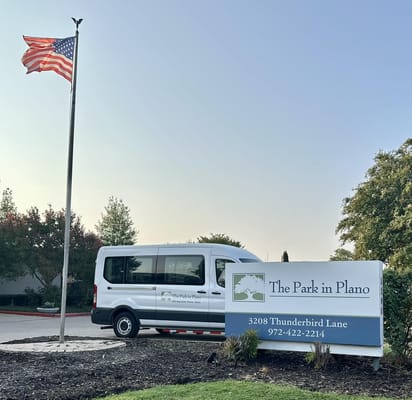 Sign of The Park in Plano with a van and American flag