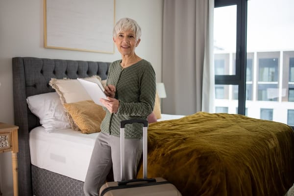 Senior woman standing in a bright room with luggage