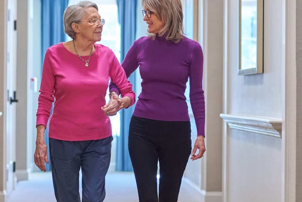 Resident and staff member walking in a facility hallway