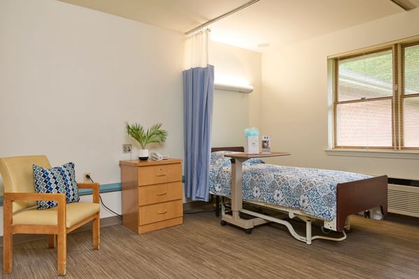 A furnished private resident room with a bed and chair