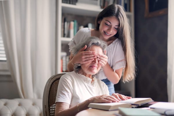 A young girl playfully covering an older woman's eyes