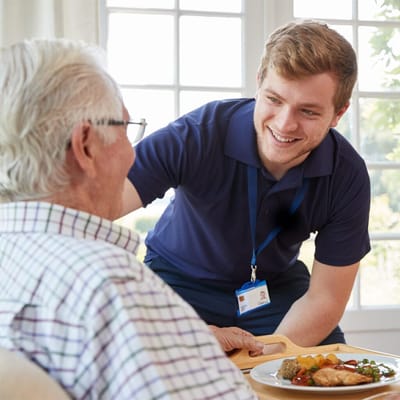 Staff serving food to a resident in a bright room