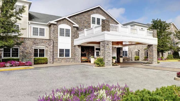 The entrance of Atria Rye Brook with stone facade and flower beds.
