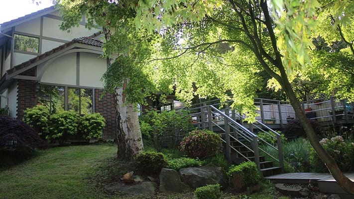 Sunny exterior of Crystal Falls Adult Family Home with landscaped garden and stairs