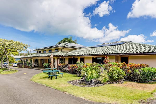 A building exterior of Kīnā ‘Ole Estate surrounded by greenery