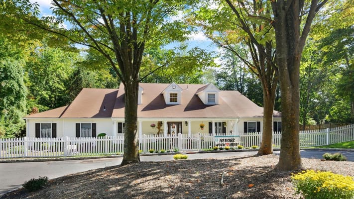 A charming white building with a porch and a picket fence surrounded by trees.